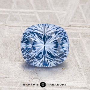 A 1.62-carat cushion-cut Ceylon Sapphire with intricate facets rests on a textured, light surface. The Earth's Treasury logo is shown below.