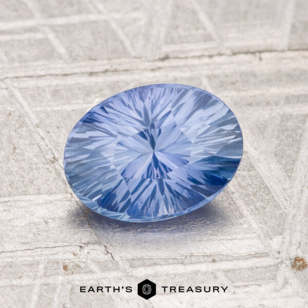 1.49-Carat Ceylon Sapphire A 1.49-carat Ceylon sapphire with an oval cut and starburst facets rests on a textured metallic surface. "Earth's Treasury" appears at the bottom.