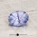 A 1.45-carat Ceylon sapphire, cut in an oval facet with a light lavender-blue hue, rests on a textured light gray surface. The "Earth's Treasury" logo appears at the bottom.