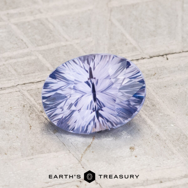 1.45-Carat Ceylon Sapphire A 1.45-carat Ceylon sapphire, cut in an oval facet with a light lavender-blue hue, rests on a textured light gray surface. The "Earth's Treasury" logo appears at the bottom.