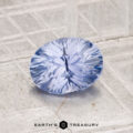 A faceted 1.45-carat Ceylon Sapphire with a starburst pattern rests on a textured gray surface, with the "Earth's Treasury" logo displayed at the bottom.