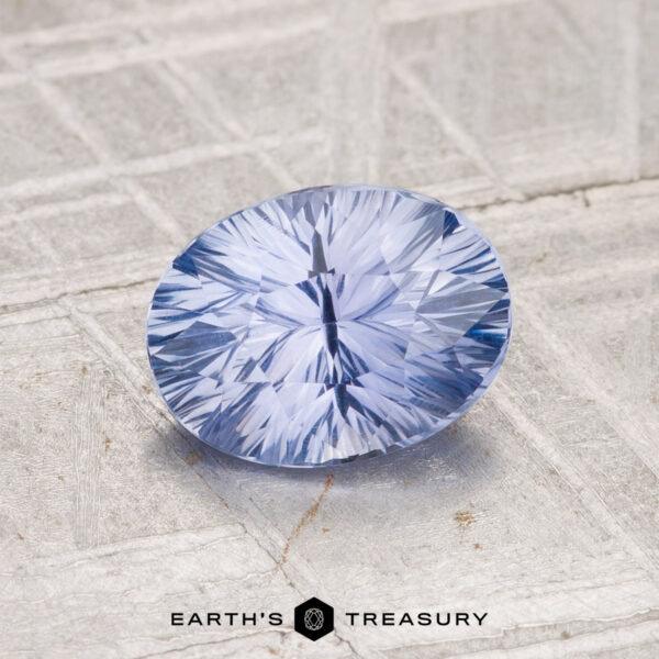 1.45-Carat Ceylon Sapphire A faceted 1.45-carat Ceylon Sapphire with a starburst pattern rests on a textured gray surface, with the "Earth's Treasury" logo displayed at the bottom.
