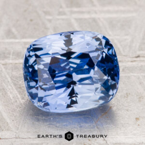 A 4.62-carat Ceylon sapphire with a cushion cut rests on a metallic textured surface, with the text "Earth's Treasury" displayed at the bottom of the image.