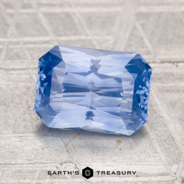 2.54-Carat Ceylon Sapphire A 2.54-carat Ceylon sapphire with faceted edges sits on a textured gray surface; "EARTH'S TREASURY" appears at the bottom.