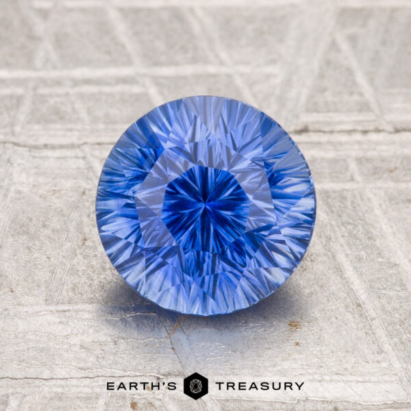 2.04-Carat Ceylon Sapphire (Heated) A 2.04-carat heated Ceylon sapphire, round and brilliant-cut, is showcased on a textured metallic surface with "Earth's Treasury" shown at the bottom.