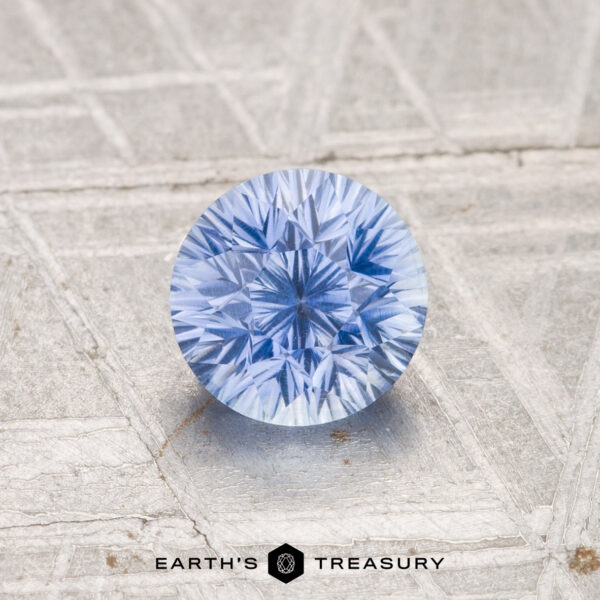 1.14-Carat Ceylon Sapphire (Heated) A 1.14-carat heated Ceylon sapphire, round and brilliant-cut, is showcased on a textured metallic surface with "EARTH'S TREASURY" at the bottom center.