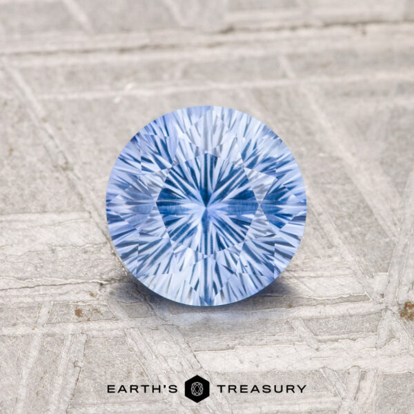 1.05-Carat Ceylon Sapphire (Heated) A 1.05-carat, brilliantly-cut Ceylon sapphire (heated) rests on a textured gray surface with the "EARTH'S TREASURY" logo at the bottom.