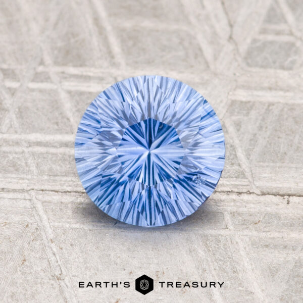 1.26-Carat Ceylon Sapphire (Heated) A round, brilliant-cut 1.26-Carat Ceylon Sapphire (Heated) rests on a textured light gray surface, with "EARTH’S TREASURY" displayed below.