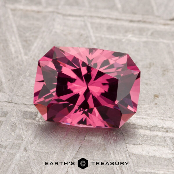 2.24-Carat Tanga Garnet A 2.24-carat faceted rectangular Tanga Garnet gemstone in vivid pink is displayed on a textured light gray surface with "EARTH'S TREASURY" text at the bottom.