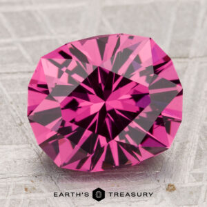 A 5.18-carat oval Tanga Garnet is displayed on a textured gray surface with the text "Earth's Treasury" below.