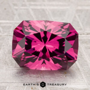 A 4.38-carat Tanga Garnet with a radiant cut and intricate facets is showcased on a textured surface, with "EARTH'S TREASURY" visible below.