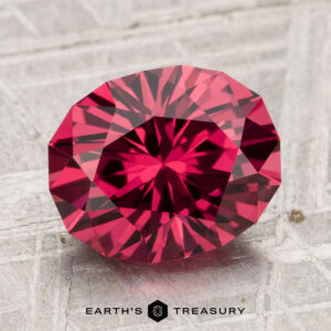 A 3.91-carat Tanga Garnet, round and faceted, is displayed on a textured gray surface with the "Earth's Treasury" logo below.