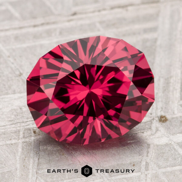 3.91-Carat Tanga Garnet A 3.91-carat Tanga Garnet, round and faceted, is displayed on a textured gray surface with the "Earth's Treasury" logo below.