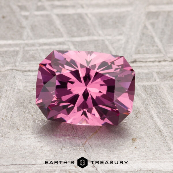 1.80-Carat Tanga Garnet A 1.80-carat Tanga Garnet, cut in a faceted rectangular shape, is displayed on a textured gray surface with the "Earth's Treasury" logo at the bottom.
