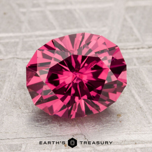 3.27-Carat Tanga Garnet A 3.27-carat Tanga Garnet, round with a brilliant faceted cut, is displayed on a textured gray surface with the "Earth's Treasury" logo at the bottom.