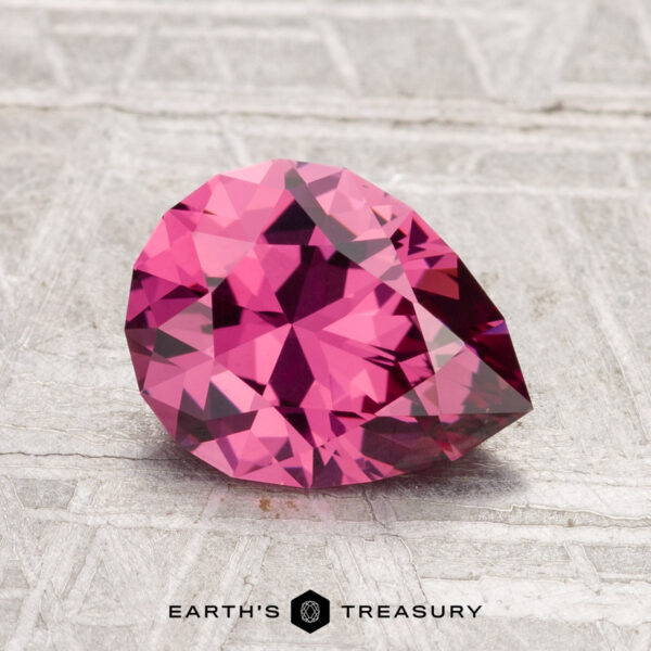 1.73-Carat Tanga Garnet A 1.73-carat Tanga Garnet, pear-shaped and faceted in pink, sits on a textured gray surface with "EARTH'S TREASURY" displayed at the bottom.