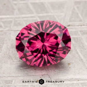 A 2.80-carat, oval-cut Tanga garnet in vivid pink is showcased on a textured surface, with the "Earth's Treasury" logo at the bottom of the image.