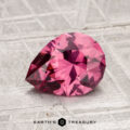 A faceted, pear-shaped 1.54-carat Tanga Garnet gemstone rests on a textured, light-colored surface with "Earth's Treasury" printed below.