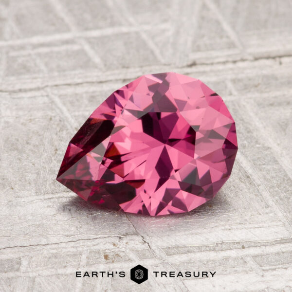 1.54-Carat Tanga Garnet A faceted, pear-shaped 1.54-carat Tanga Garnet gemstone rests on a textured, light-colored surface with "Earth's Treasury" printed below.
