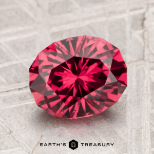 A 2.76-carat Tanga Garnet, faceted in an oval cut, displayed on a textured gray surface with the text "Earth's Treasury" at the bottom.