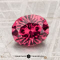 A 2.51-carat Tanga Garnet, faceted in an oval cut, is displayed on a textured, light surface with "Earth's Treasury" beneath it.