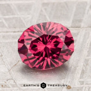 A 2.51-carat Tanga Garnet, faceted in an oval cut, is displayed on a textured, light surface with "Earth's Treasury" beneath it.