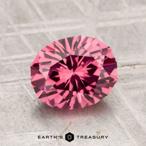2.36-Carat Tanga Garnet A 2.36-carat Tanga Garnet, round and brilliant-cut, is showcased on a textured gray surface with "EARTH'S TREASURY" displayed below.