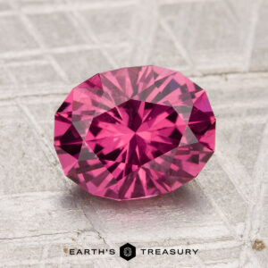 2.29-carat oval-cut Tanga Garnet with detailed facets, shown on a textured silver-gray surface, with "Earth's Treasury" text below.