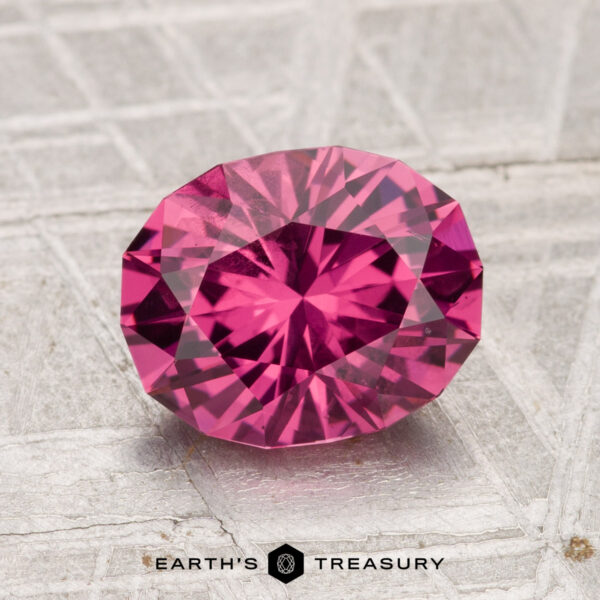 2.29-Carat Tanga Garnet 2.29-carat oval-cut Tanga Garnet with detailed facets, shown on a textured silver-gray surface, with "Earth's Treasury" text below.