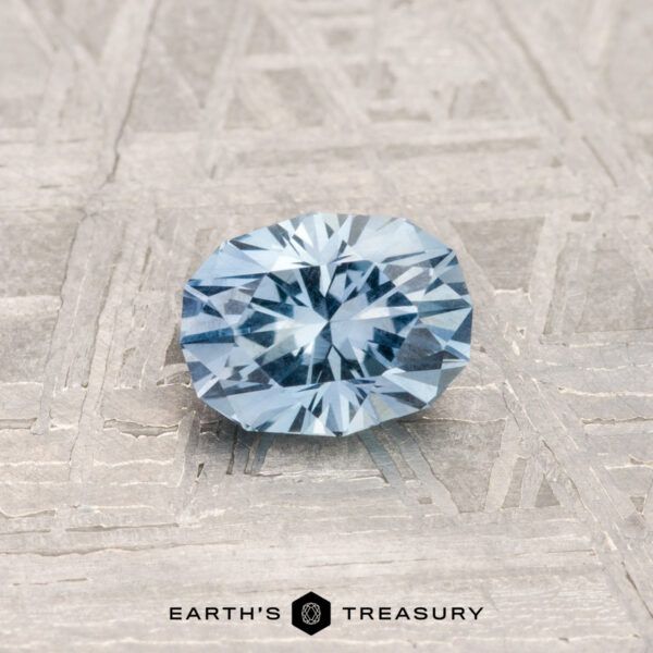 0.72-Carat Montana Sapphire A 0.72-carat, round brilliant Montana sapphire sits on a textured metal surface with "EARTH'S TREASURY" displayed at the bottom.