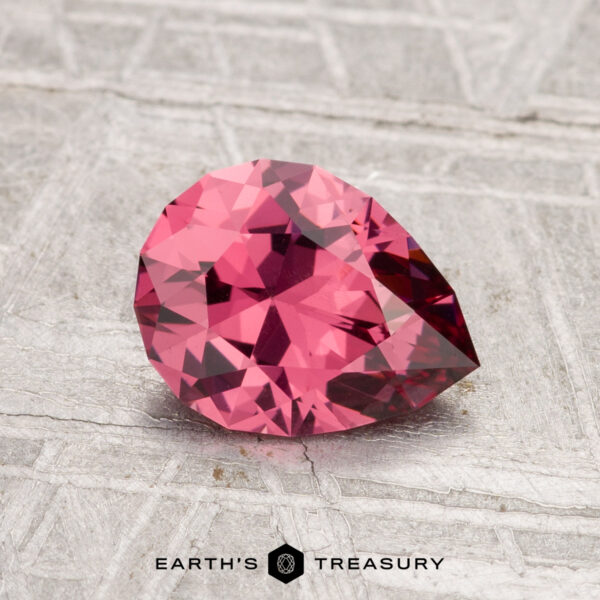 1.22-Carat Tanga Garnet A 1.22-carat faceted pear-shaped Tanga garnet gemstone displayed on a textured gray surface with "EARTH'S TREASURY" text at the bottom.