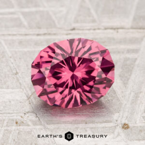 A faceted, oval-shaped 1.92-carat Tanga Garnet is displayed on a textured gray surface, with the words "EARTH'S TREASURY" below.