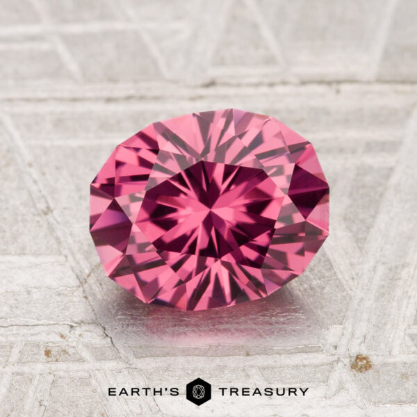 1.92-Carat Tanga Garnet A faceted, oval-shaped 1.92-carat Tanga Garnet is displayed on a textured gray surface, with the words "EARTH'S TREASURY" below.
