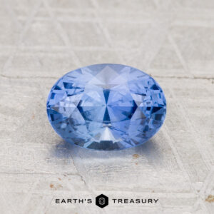 A faceted oval 1.78-carat Ceylon Sapphire rests on a textured surface, with the "Earth's Treasury" logo visible at the bottom of the image.