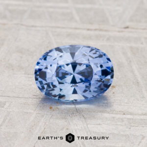 A 1.18-carat Ceylon sapphire, faceted in an oval shape, displayed on a textured light surface with the "EARTH'S TREASURY" logo and text at the bottom.