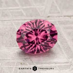 A 1.77-carat Tanga Garnet, expertly faceted in an oval cut, rests on a textured gray surface featuring the "Earth's Treasury" logo below.