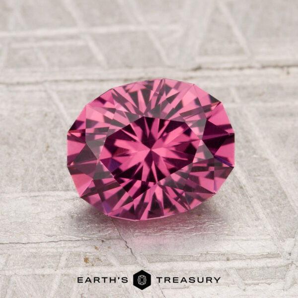 A 1.77-carat Tanga Garnet, expertly faceted in an oval cut, rests on a textured gray surface featuring the "Earth's Treasury" logo below.