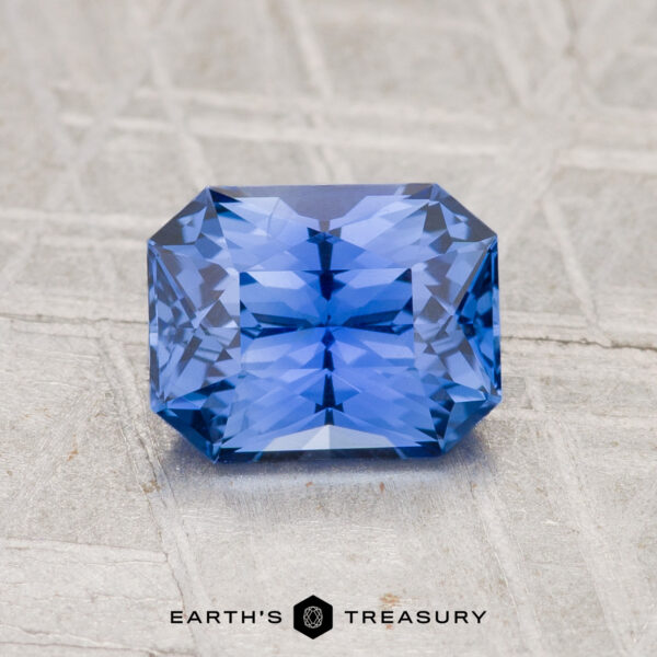 1.41-Carat Ceylon Sapphire A 1.41-carat, rectangular cornflower blue Ceylon Sapphire rests on a light textured surface with "EARTH'S TREASURY" below.