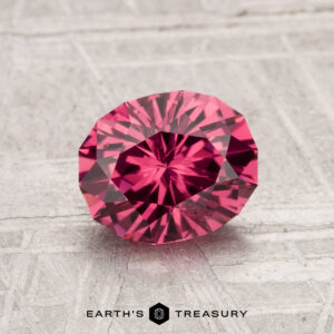 The 1.49-Carat Tanga Garnet, a round faceted pink gemstone, is displayed on a light textured surface with "Earth's Treasury" at the bottom.