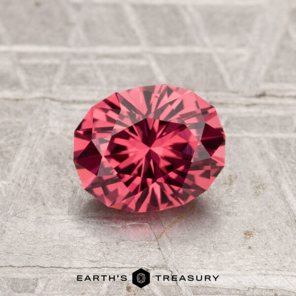 1.19-Carat Tanga Garnet A 1.19-carat Tanga Garnet, an oval faceted pink gemstone, is showcased on a textured surface with the words "EARTH'S TREASURY" at the bottom.