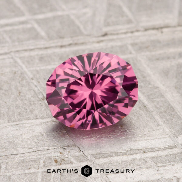 A 1.19-carat faceted oval Tanga Garnet rests on a textured metallic surface, with "EARTH'S TREASURY" displayed at the bottom of the image.