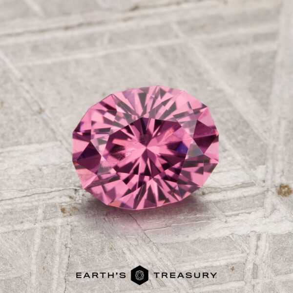 A 1.12-carat oval Tanga Garnet is displayed on a textured light gray surface, with "EARTH'S TREASURY" at the bottom.