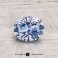 A 1.27-carat heated Montana sapphire, faceted in an oval cut, is displayed on a textured, light surface with "EARTH'S TREASURY" below.