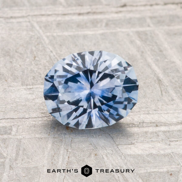 1.27-Carat Montana Sapphire (Heated) A 1.27-carat Montana Sapphire (Heated) with an oval cut is displayed on a textured light gray surface, with "EARTH’S TREASURY" written at the bottom.
