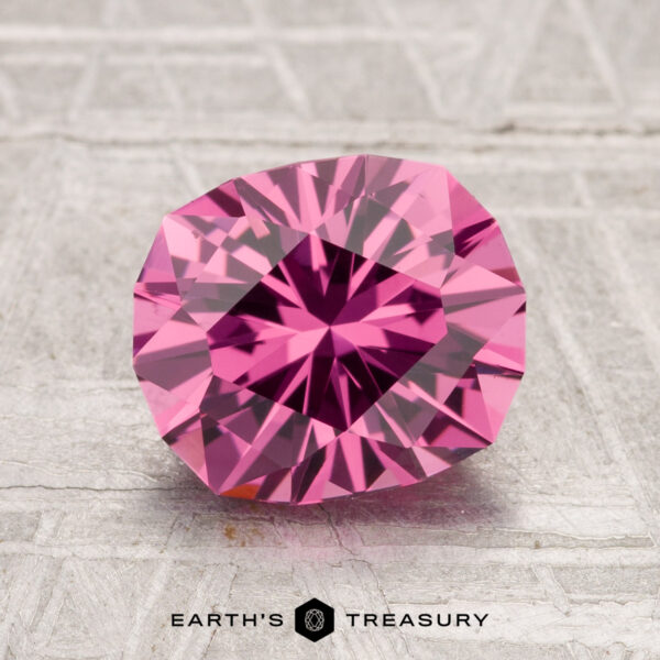 2.41-Carat Tanga Garnet A 2.41-carat Tanga Garnet gemstone with a pink hue is displayed on a textured gray surface, featuring the text "EARTH'S TREASURY" at the bottom.