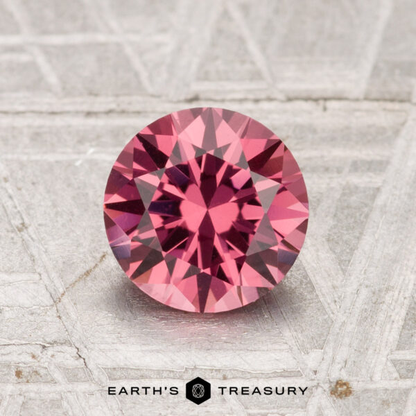 1.32-Carat Tanga Garnet A 1.32-carat Tanga Garnet with a round cut is displayed on a textured gray surface, featuring the text "EARTH'S TREASURY" at the bottom.