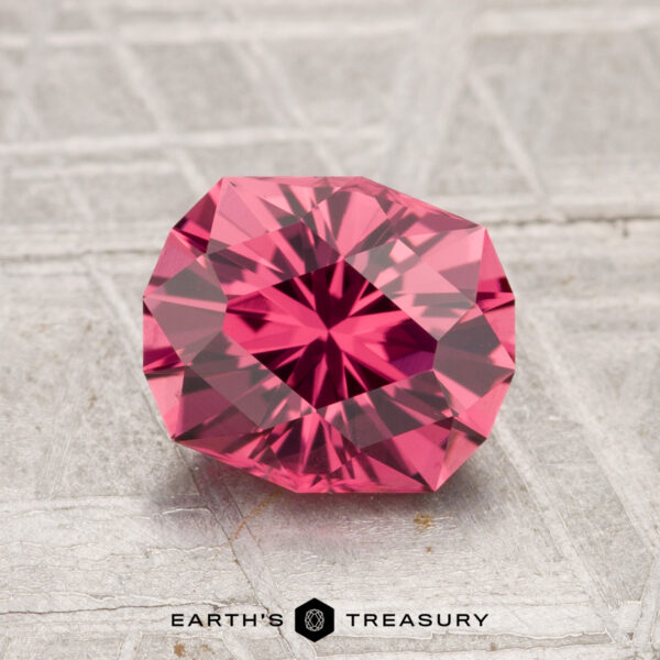 1.82-Carat Tanga Garnet A 1.82-carat Tanga Garnet, round and faceted with a vivid pink hue, rests on a textured silvery surface, accompanied by the "Earth's Treasury" text below.