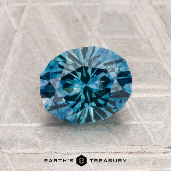 1.81-Carat Montana Sapphire (Heated) A 1.81-carat heated Montana sapphire, round brilliant-cut and blue, is shown on a textured gray surface with "EARTH'S TREASURY" displayed at the bottom.