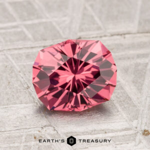 A 1.66-carat Tanga Garnet, faceted in a geometric cut, is displayed on a textured gray surface. The Earth's Treasury logo is visible at the bottom.