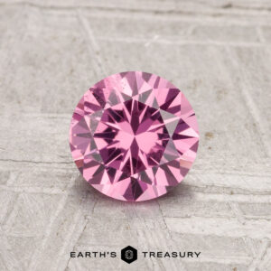 A round, faceted 0.98-carat Tanga Garnet gemstone is displayed on a light gray textured background with the text "EARTH'S TREASURY" beneath it.